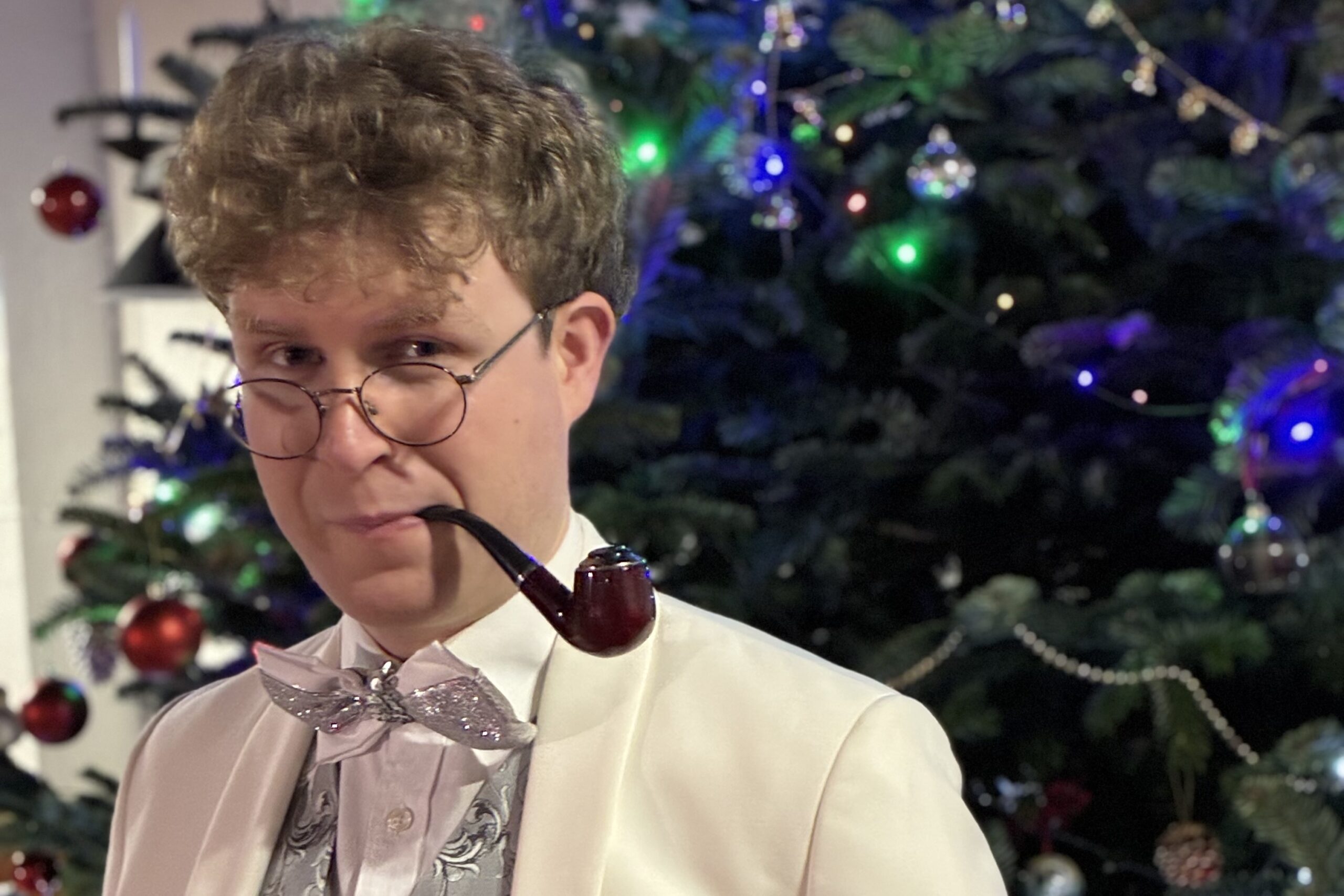 Man wearing white waistcoat with pipe in front of Christmas tree